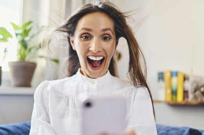 Frau freut sich und hält ihr Handy in der Hand