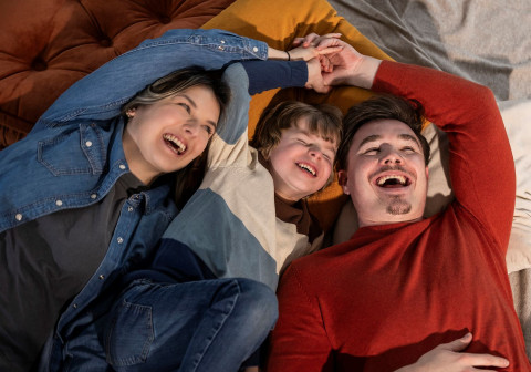 Wir arbeiten Hand in Hand mit den LBS-Finanzierungsexperten Vater, Mutter und Sohn liegen lachend auf dem Boden.